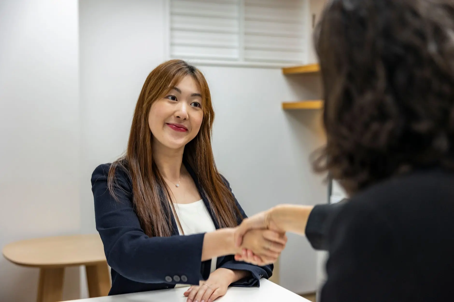 2026년 중소기업 특별채용 지원금 관련 이미지 - Businesswoman in professional attire shaking hands with recruiter in an office setting.